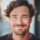 Homme souriant avec une barbe et des cheveux bouclés.